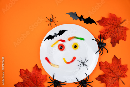 White plate with funny face made of gummy candies: jelly eyes, gummy worms. Halloween party, Halloween celebration, table setting, spooky decoration, creative serving, Halloween food idea. Top view.
