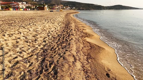 High-resolution aerial drone image showcasing a picturesque beachfront resort scene. Neatly arranged white umbrellas and lounge chairs line the golden sandy shore, while colorful hotel buildings with 