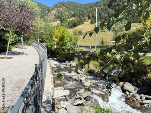 Sendero pavimentado con una banderilla metálica junto a un río con agua 