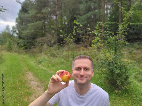 Smiling man holding one nectarine against a outdoor background