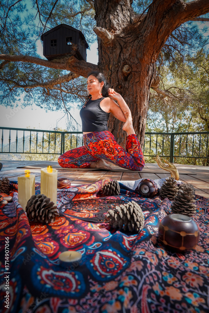 Fototapeta premium Woman practicing yoga pose outdoors on wooden deck under a tree