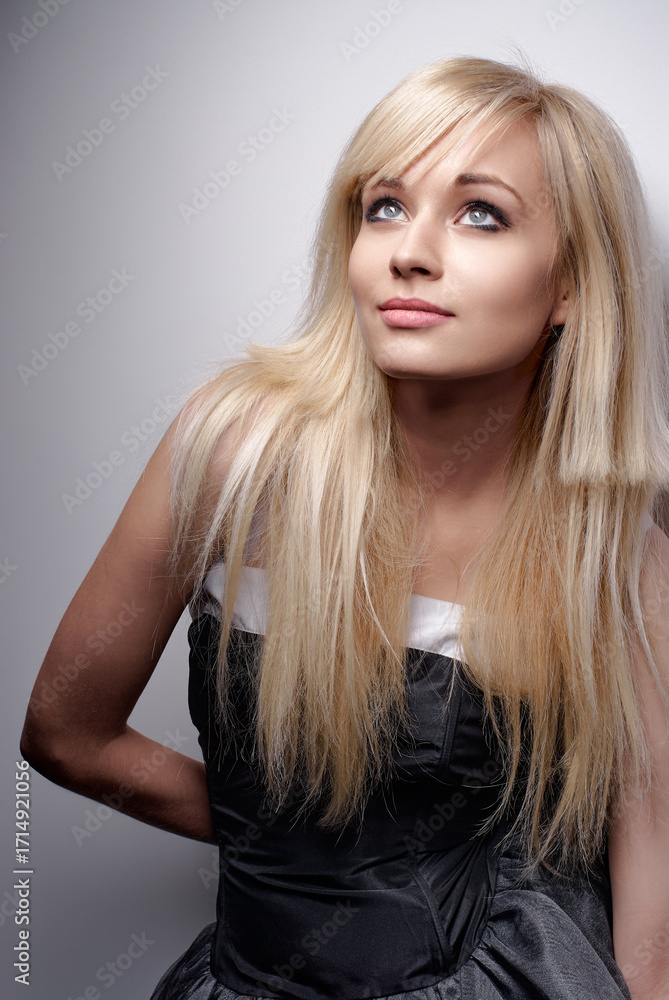 Naklejka premium A captivating portrait of a stylish woman with blonde hair, showcased in elegant studio lighting and wearing a sophisticated black dress that perfectly highlights her graceful features.