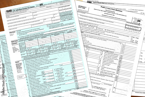 Tax year 2025 IRS 1040 and schedule c, profit or loss from business, forms lay on a desktop.