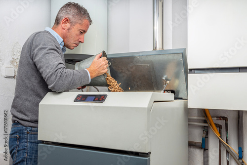 Man filling biomass boiler hopper with wood pellets for home heating with copy space.