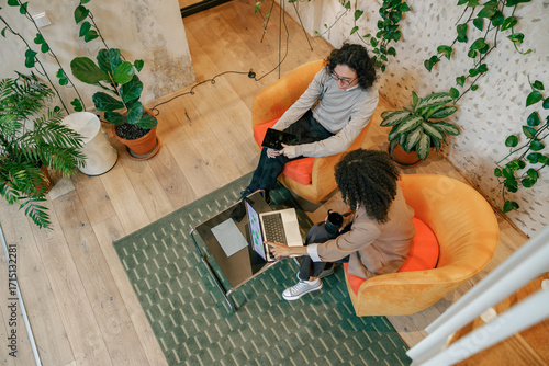 Two individuals are engaged in a collaborative discussion within a modern office space filled with various plants