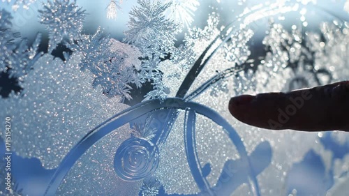 Finger touching frosty glass with traced snowflake shapes and patterns  