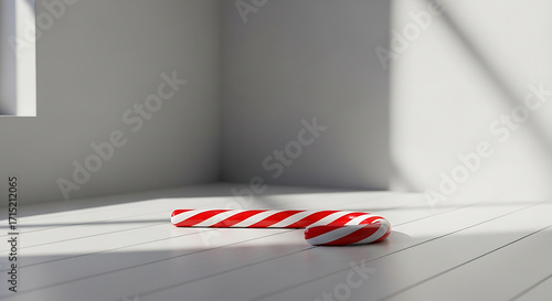 A candy cane rests on a white wooden floor in a bright, minimalist room with a window.