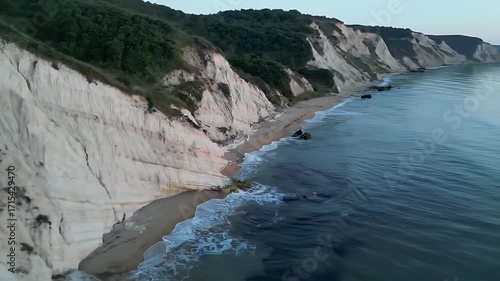 Coastal cliff face at sunrise, displaying layered rock formations and gentle ocean waves.