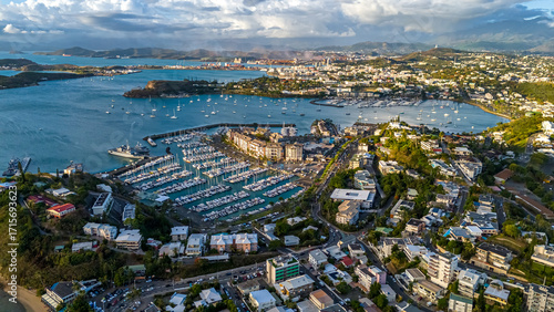 An aerial drone view focusing on the bustling marina in Nouméa, New Caledonia. Hundreds of yachts and sailboats are docked in the harbor against the city backdrop
