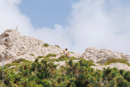 A teeny boy sits on rocky limestone peak against blue sky
