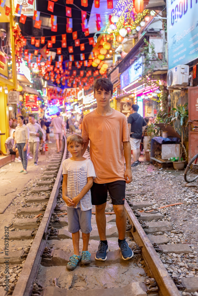 Obraz premium Train street in Hanoi in the evening. Child posing on the railway in Hanoi, train passing very close to the cafe shops