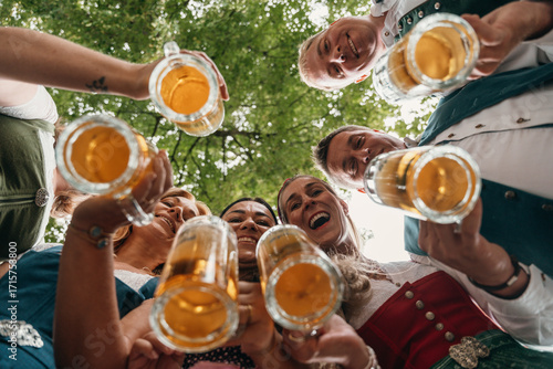 Cheerful friends in Bavarian dress enjoy Oktoberfest outdoors with beer in hand smiling low angle view of celebration