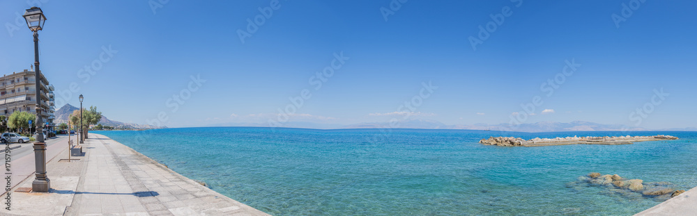 Obraz premium Blue, calm mediterranean sea at the promenade of Xylocastro, gulf of Corinth, Peloponnes, Greece (panorama)