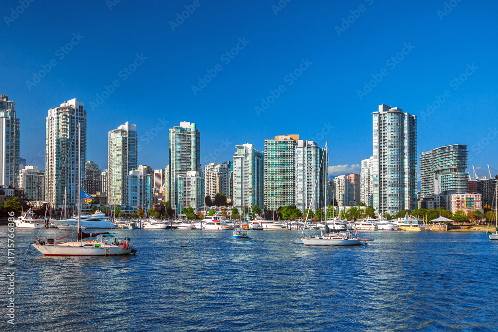 Obraz premium View of Vancouver Harbor and downtown Vancouver. A beautiful sunny day, blue water of the bay. Many boats and yachts on the foreshore, a row of skyscrapers and a blue sky