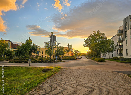 Behang quiet suburban street glows under a golden sunset sky, with soft clouds, trees,