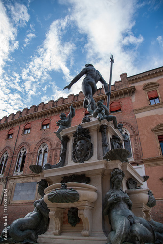 Fountain of Neptune in Bologna, Italy, under a bright blue sky dotted with fluffy white clouds