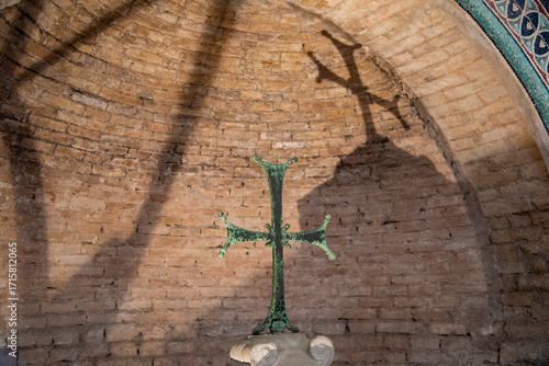 Bronze cross, prominently displayed within a brick-lined arched alcove, with its shadow projected on the curved ceiling