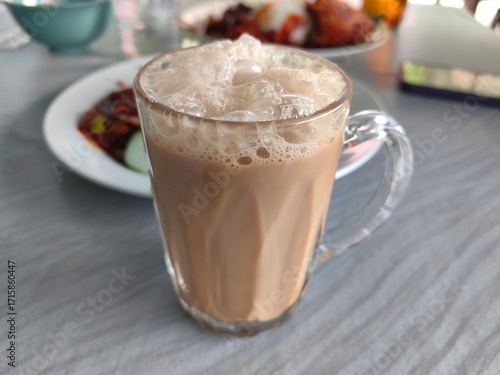 Traditional Malaysian Teh Tarik or pulled tea served in a glass with rich foam, popular hot milk tea drink in Southeast Asia and street food culture.