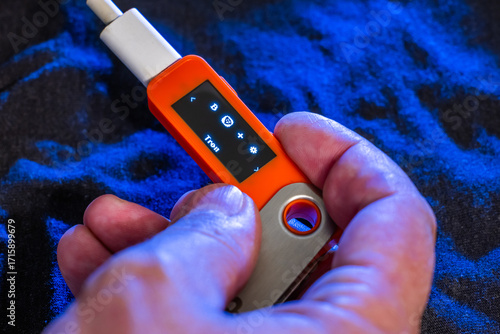 Hand holding orange hardware wallet with Tron symbol