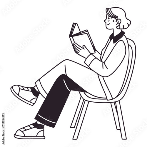 A young woman sits comfortably in a chair reading a book with a relaxed expression and crossed legs