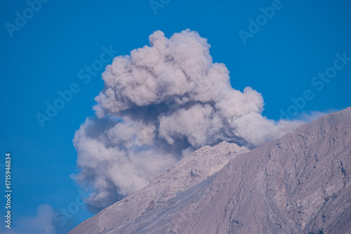 Close up view of Mount Semeru’s summit spewing smoke and volcanic ash under a bright blue sky, showcasing the natural beauty and rugged details of this powerful Indonesian volcano.