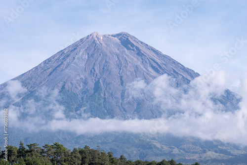 Mount Semeru’s iconic peak stands proudly against the expansive blue sky, its detailed volcanic ridges and textures clearly illuminated by daylight.