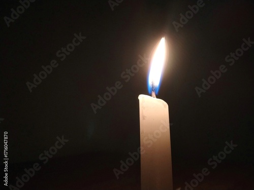 Minimalist image of a single white candle burning in a dark room. Soft warm glow symbolises hope, silence, solitude, or remembrance.