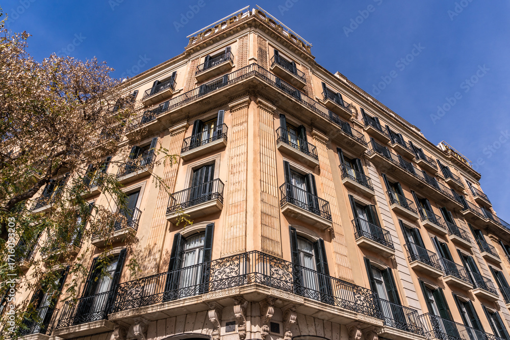 Fototapeta premium A majestic Barcelona tower block, adorned with intricate Art Nouveau architecture and windows. It stands majestically against the backdrop of a cloudy sky in its residential neighborhood.
