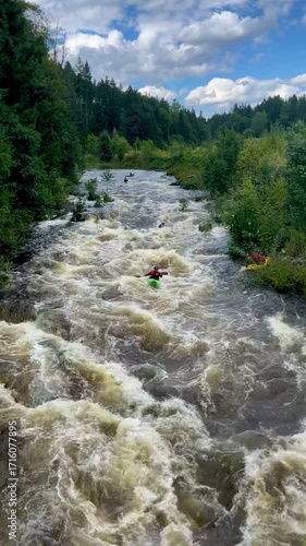 Video of tourists in kayaks paddling down a wild river with rapids. Forest and blue sky with clouds create scenic outdoor travel atmosphere.