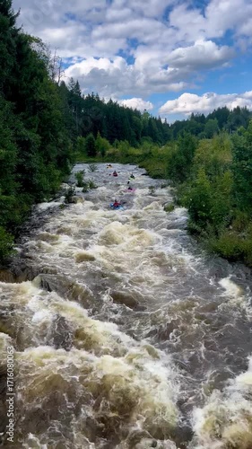 Video of several kayakers navigating fast whitewater rapids surrounded by forest. Filmed from above, showing strong current and dynamic movement.