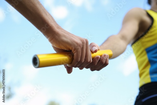 Close up hand holding yellow relay baton sports athletics teamwork competition passing handoff race.