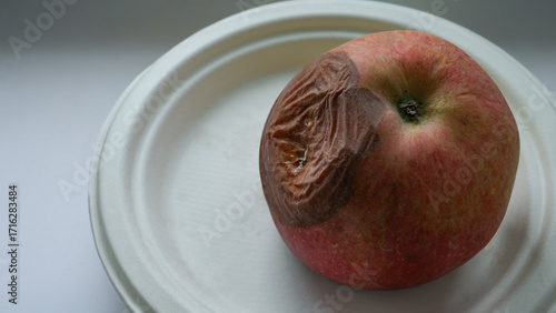 Close-up of a rotten apple with a wrinkled brown spot on a white plate.