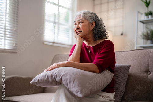 Older Asian woman deep thought home living room sofa contemplating life moments experiencing quiet reflection loneliness mental health