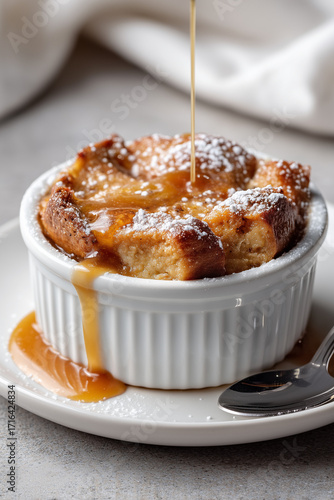 Comforting bread pudding dessert with caramel sauce in ramekin comfort shot close-up of a single topped with warm drizzle and light powdered sugar dust