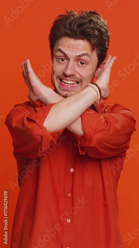 Stop, enough. Caucasian man say no hold palm folded crossed hands in finish gesture, warning of finish, prohibited access, declining communication, body language danger. Young guy on orange background