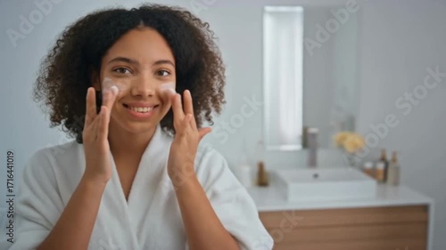 A radiant woman indulges in a self-care ritual, delicately applying a moisturizing cream to her face, her skin glowing with health and serenity.