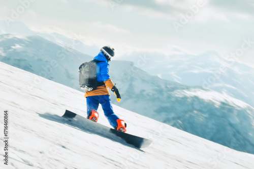 Snowboarder riding downhill on snowy slope with backpack and mountains in background on winter day