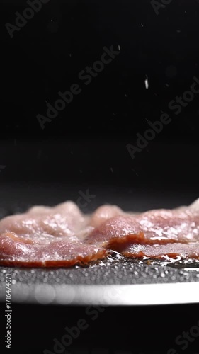 Slow motion video of bacon frying in a pan. It sizzles as it transforms from raw to a crispy, appetizing piece. Smoke rises and fat splatters during cooking.