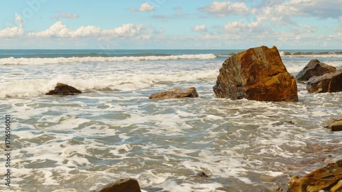 Seascape video of a stormy sea crashing against fallen rock fragments, horizon with cumulus clouds, real-time footage, copy space for nature projects
