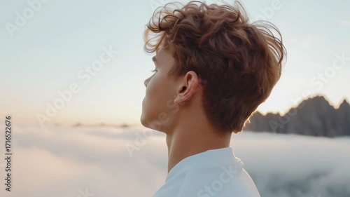 Young man on a summit above clouds with closed eyes — cinematic frame about contemplation, freedom and outdoor lifestyle.