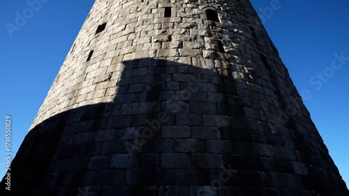 Ancient Stone Tower Architecture with Dramatic Shadows Against a Clear Blue Sky Historic Old Masonry Medieval Fortress Wall Detail on a Bright Sunny Day