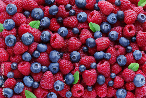 Papier peint Juicy ripe raspberries and blueberries with raspberry leaves as background, top view