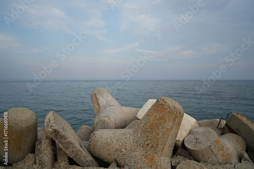 Concrete breakwaters on the Black Sea coast in Nessebar, Bulgaria. Calm seascape with blue water, cloudy sky, and coastal protection structures.