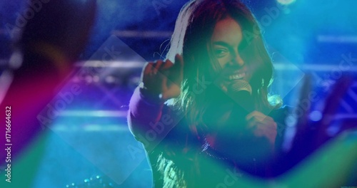 Female singer singing and pointing on center stage under vibrant lighting, with microphone and haze