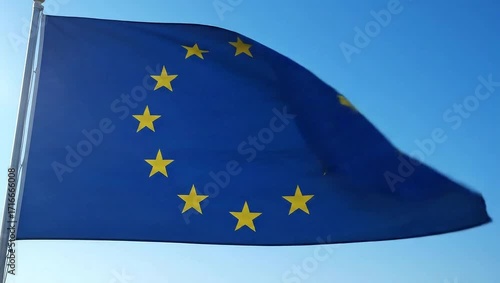  European Union flag waving in strong wind against a clear blue sky, stars glinting in sunlight