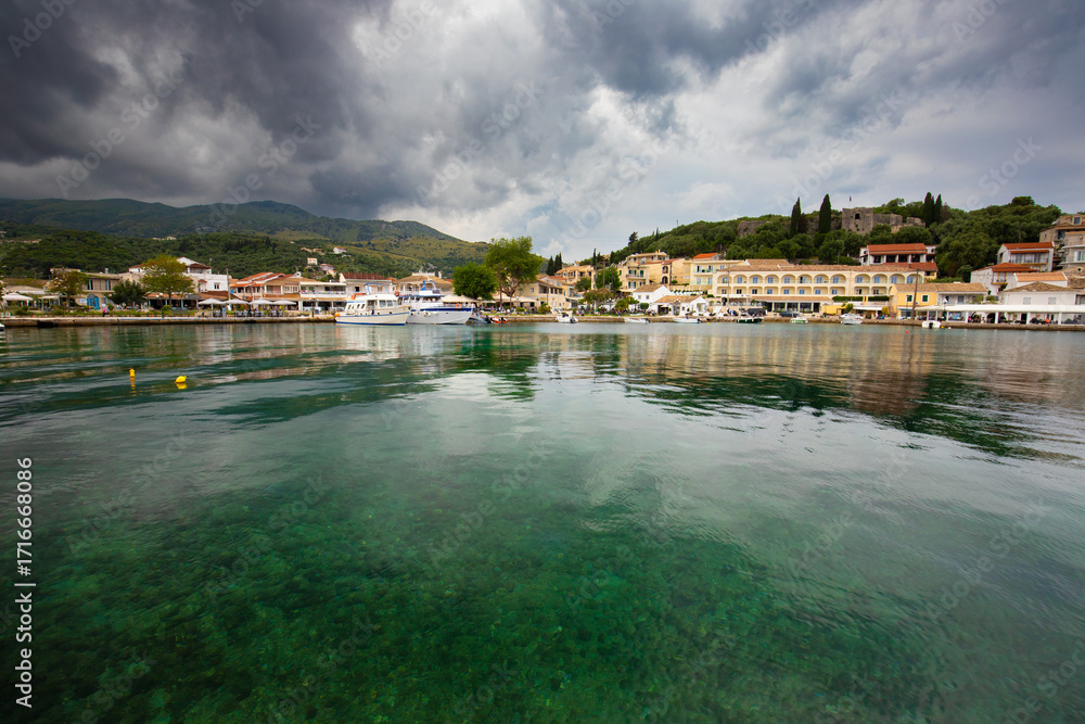 Obraz premium The picturesque harbor of Kassiopi, a charming fishing village located on the northeastern coast of the Greek island of Corfu, background or wallpaper for the project