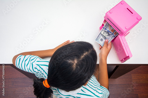 Top view of girl taking dollars from her piggy bank