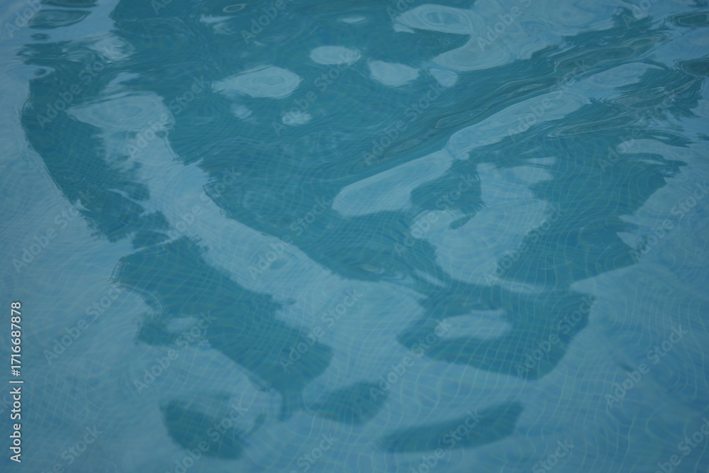 Obraz premium Blue swimming pool water surface with gentle ripples and sunlight reflections. Calm aqua texture creating a refreshing and relaxing summer atmosphere. Perfect background for vacation, spa, and wellnes