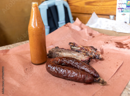 Texas BBQ smoked beef brisket and sausage with homemade sauce bottle on pink butcher paper at Luling City Market barbecue restaurant
