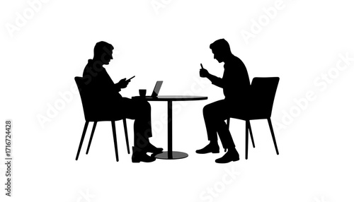 Two men sitting at a table using phones and laptop indoors  